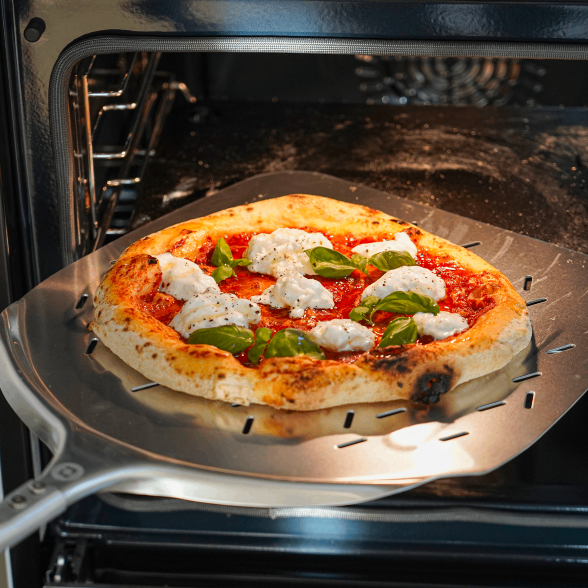 Pizza på pizzaspade på vej i ovnen